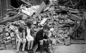Three children sit in front of rubble.