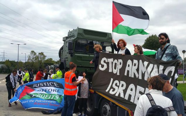 Activists stand on a military truck waving the Palestinian flag and a "Stop Arming Israel" banner.