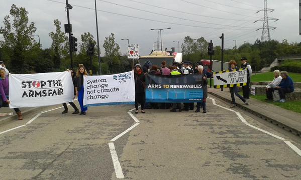 Activists blockade the road with banners reading 'Stop the Arms Fair', 'System Change Not Climate Change' and 'Arms to Renewables'