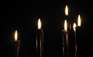 The flames of six candles stand out against a dark background