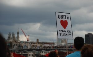 Placard with red heart on it reads, 'Unite today for Turkey'. Held against the London skyline, against a cloudy sky