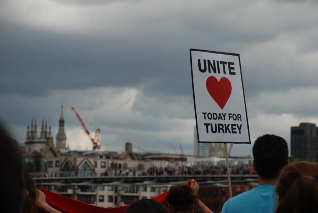 Placard with red heart on it reads, 'Unite today for Turkey'. Held against the London skyline, against a cloudy sky