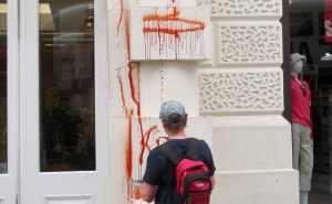 A person stands in front of a white building which is covered in red paint