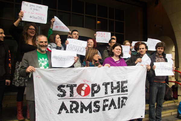 A group of activists stand in a group with a 'Stop the Arms Fair' banner