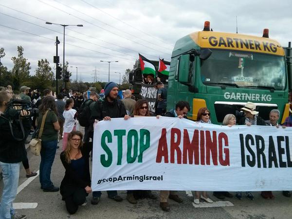 Activists hold a 'Stop Arming Israel' banner in front of an armoured vehicle
